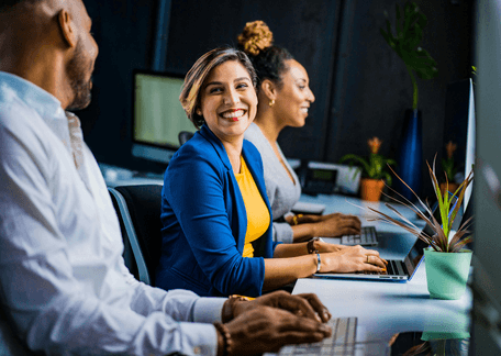Woman smiling while working on laptop with colleagues